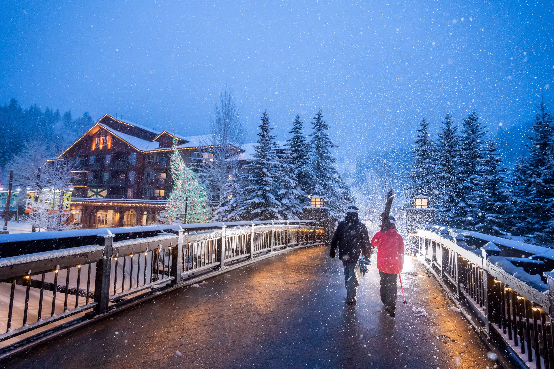 Skiers walk across Creekside Bridge with Legends Hotel behind